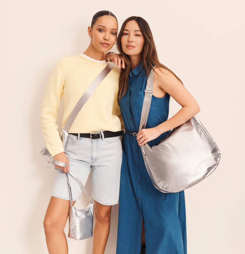 Two women posing in neutral-toned outfits while carrying metallic silver shoulder and crossbody bags.