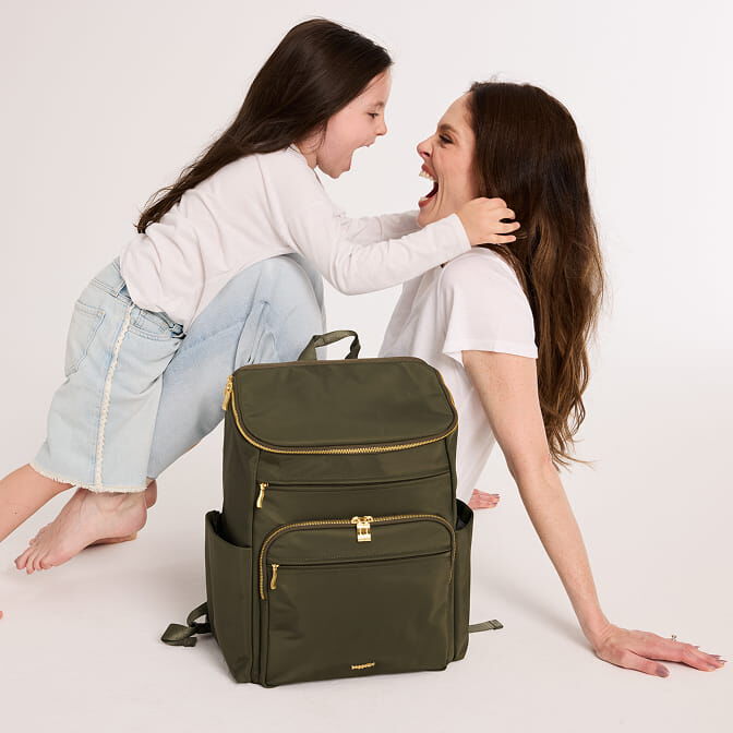 Coco Rocha and her daughter laughing together beside an olive green Baggallini backpack.