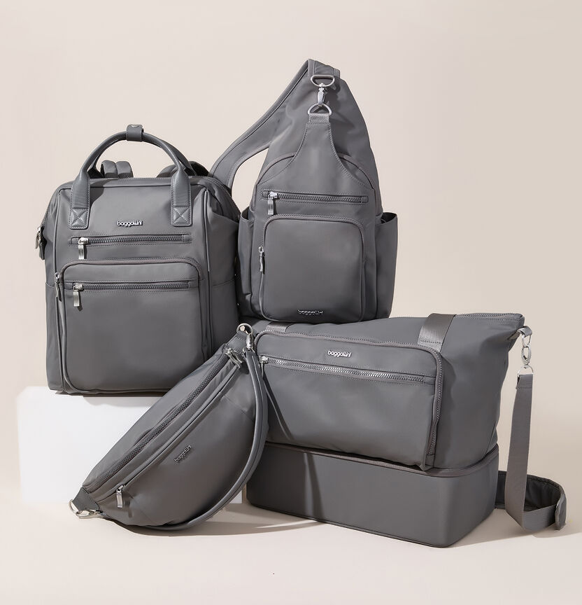 Collection of gray Baggallini bags, including a backpack, sling bags, and crossbody bag, arranged against a neutral background.