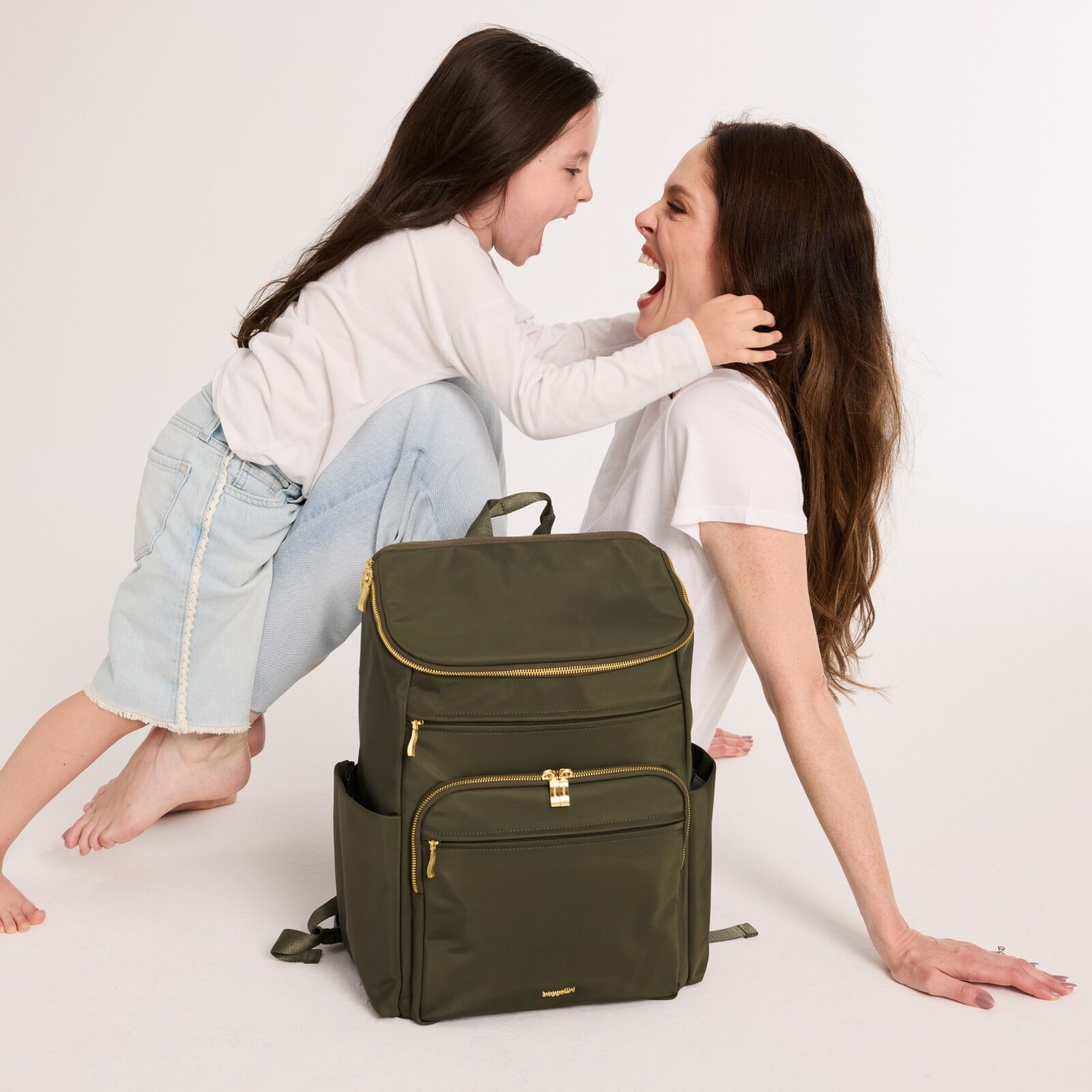 Coco Rocha and her daughter laughing together beside an olive green Baggallini backpack.