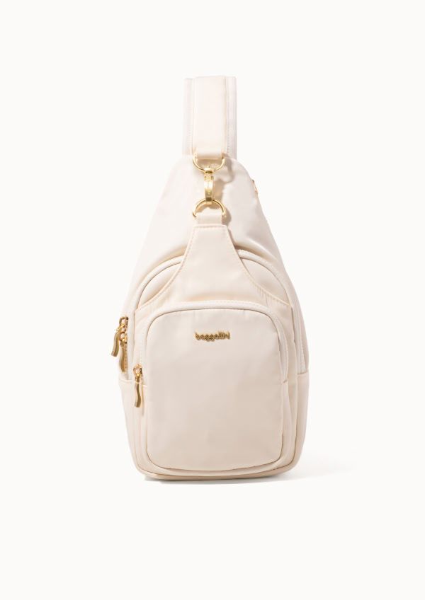 A cream crossbody bag with gold-tone hardware, multiple zippered compartments, and a front utility pocket